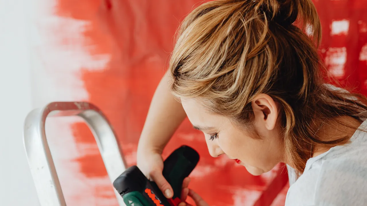 A woman drilling while standing on a ladder.